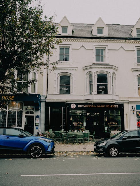 A street scene showing a white three-storey building with large bay windows and decorative architectural details, housing a shop called 'Botanical Babe Plants' on the ground floor, which features an o